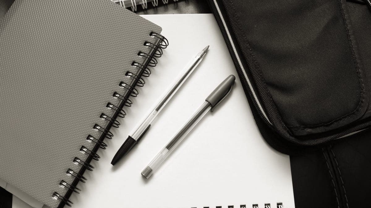 An open notebook with a pen beside a stack of books