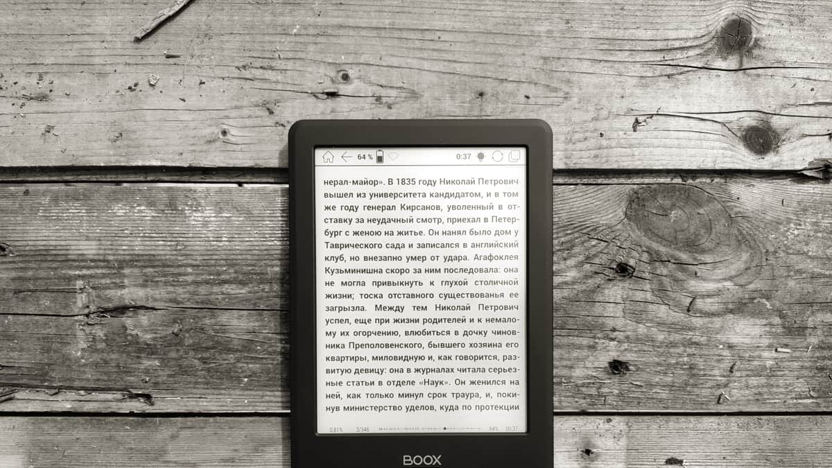 An e-reader resting on a table beside a printed book